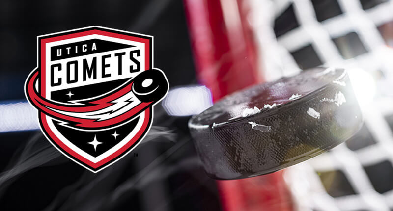 A close-up of an ice hockey puck in mid-air of a goal net with flare from the arena lights.