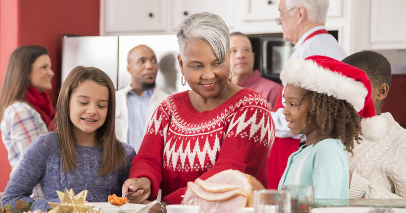 Multi-ethnic group of family members work together in a crowded kitchen to prepare dinner for a family Christmas celebration.