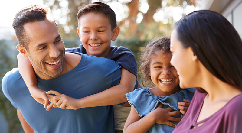 Smiling Family With Parents Giving Children Piggyback Rides