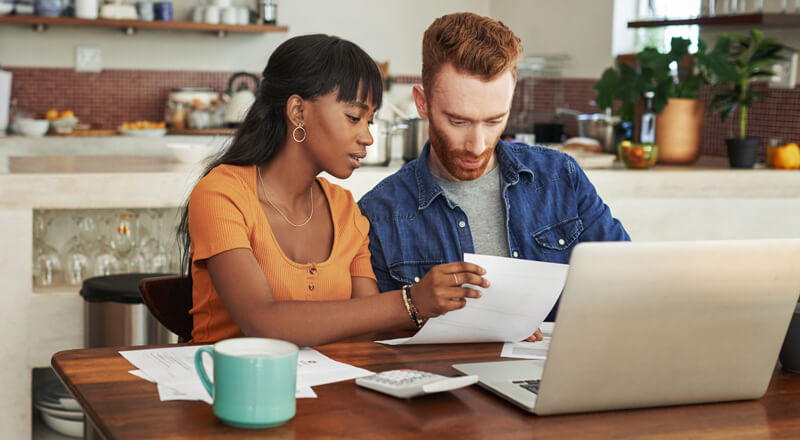 Couple reviewing paperwork while sitting with their laptop