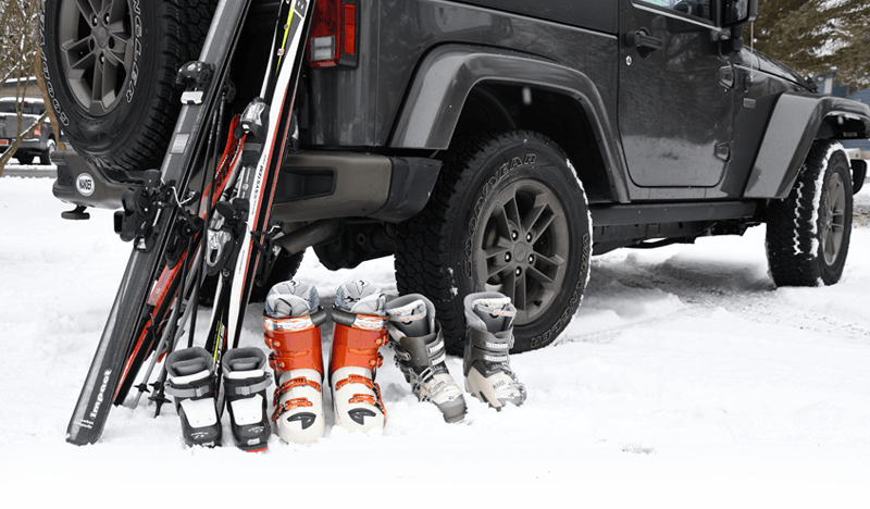Skis, boots, and poles rest against a Jeep as family prepares for their financed ski vacation