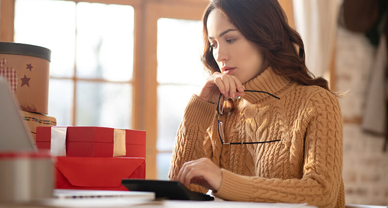 Woman in knitted sweater sitting at the table and making calculations.