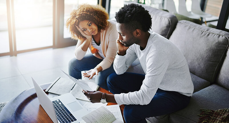 Young couple studies their debt paperwork with computer and bills, debating debt consolidation versus settlement.