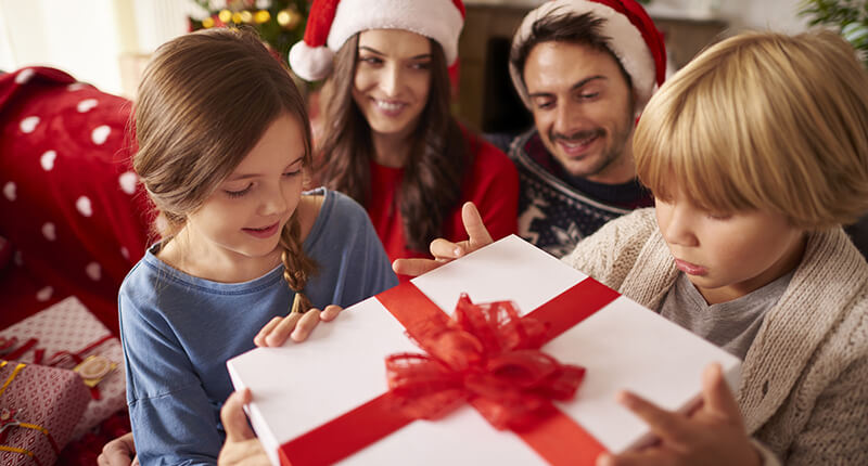 Children open a present as their parents watch, enjoying a holiday assisted by Holiday Loan financing