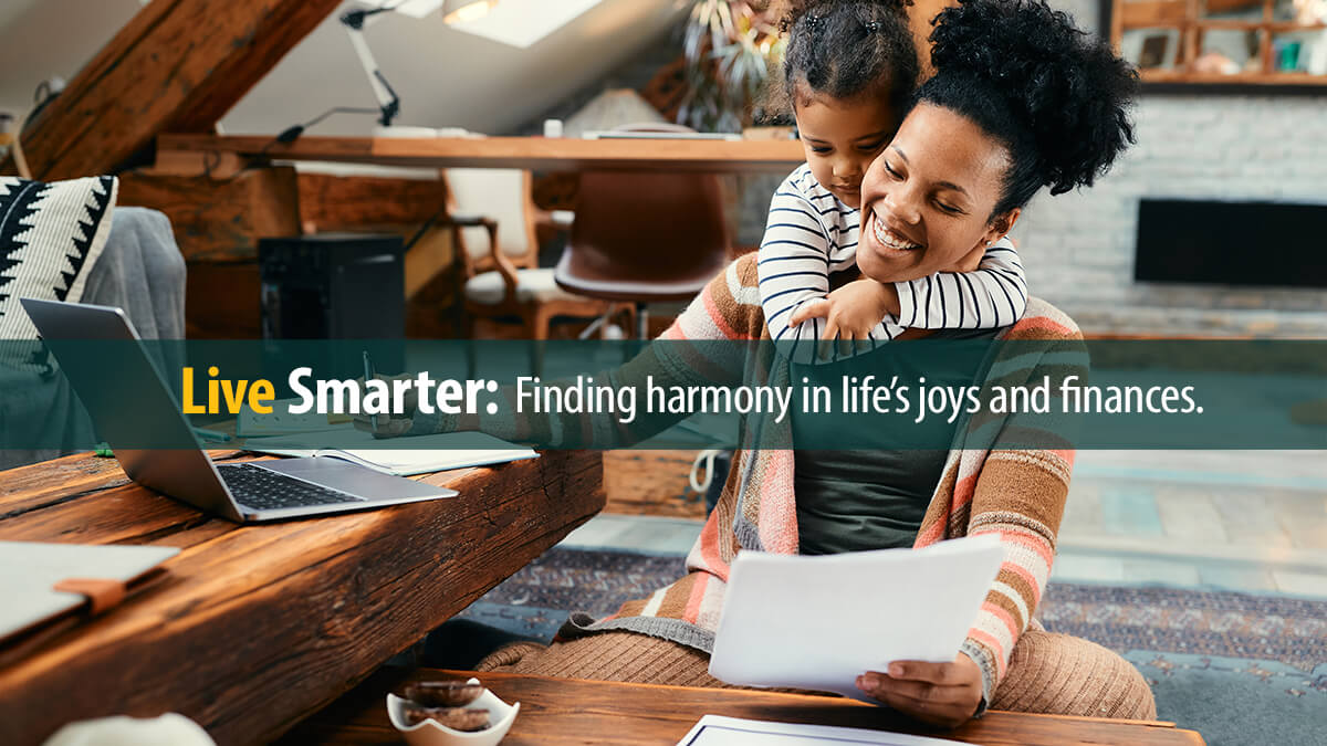 Happy African American mother using laptop and working on paperwork while her daughter is embracing her at home.