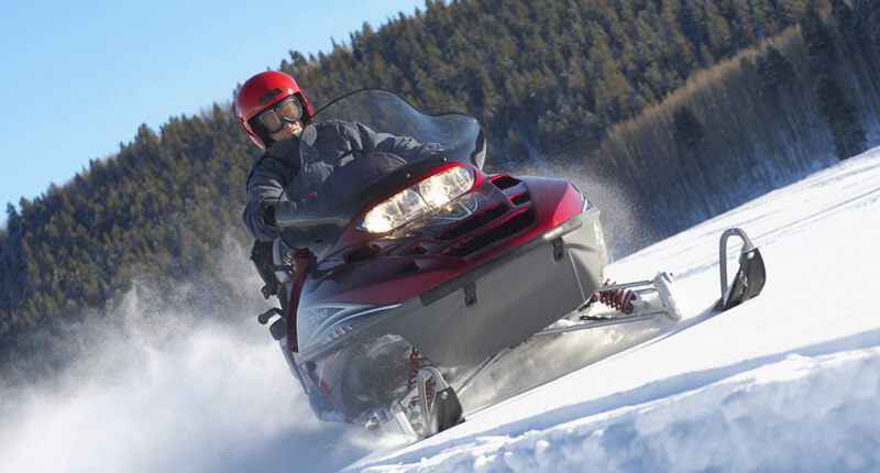 A man rides his snowmobile, financed through First Source, across a snowy field