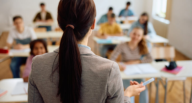 Back view of female teacher giving a lecture to group of high school students in the classroom.